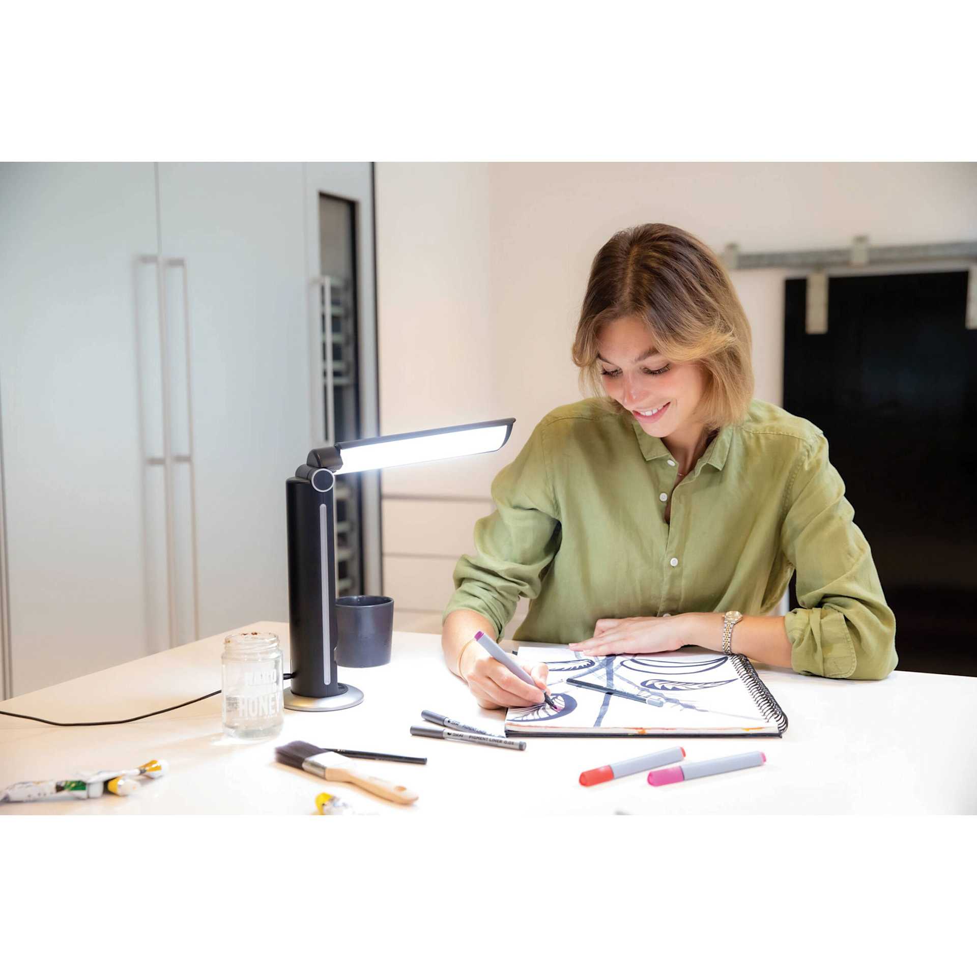 Daylight TwoSun Light Therapy Task Lamp, adult using the lamp on a desk to draw