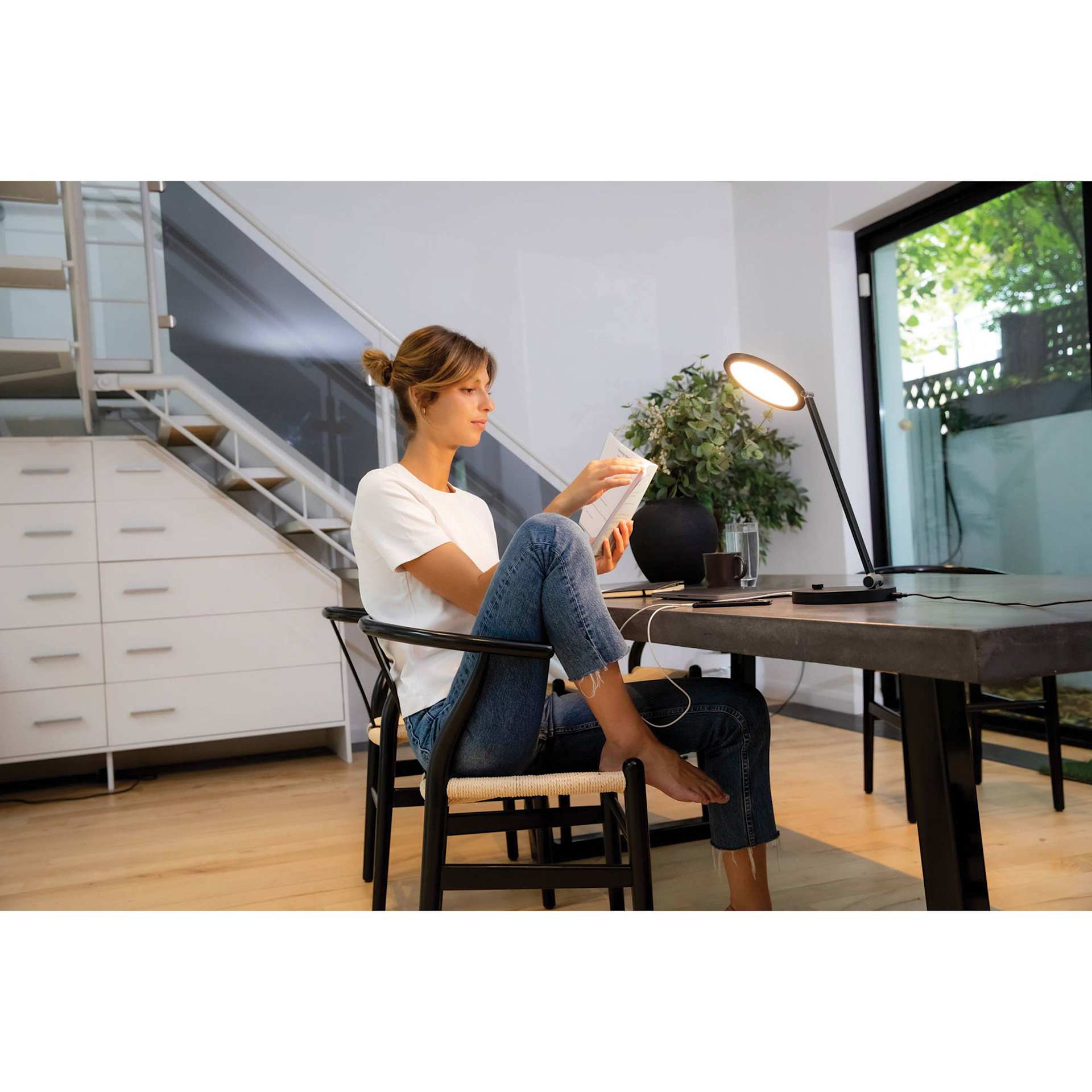 Daylight TriSun Light Therapy Desk Lamp, warm light on pointing to an adult reading a book