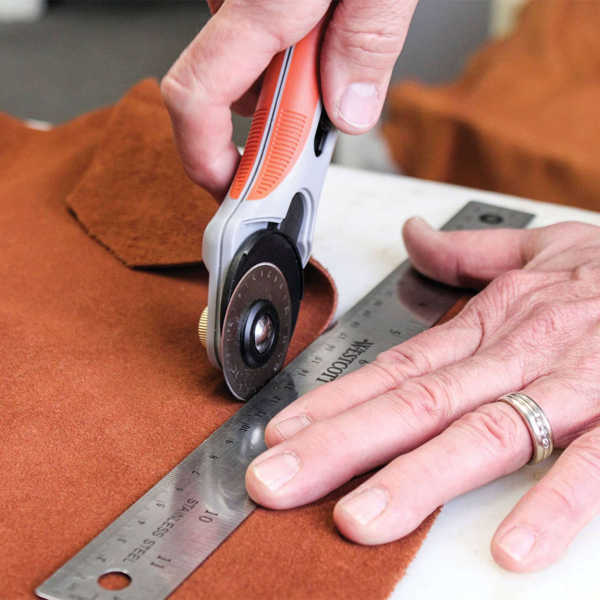 Realeather Leather Rotary Cutter, hand using blade on fabric with a ruler