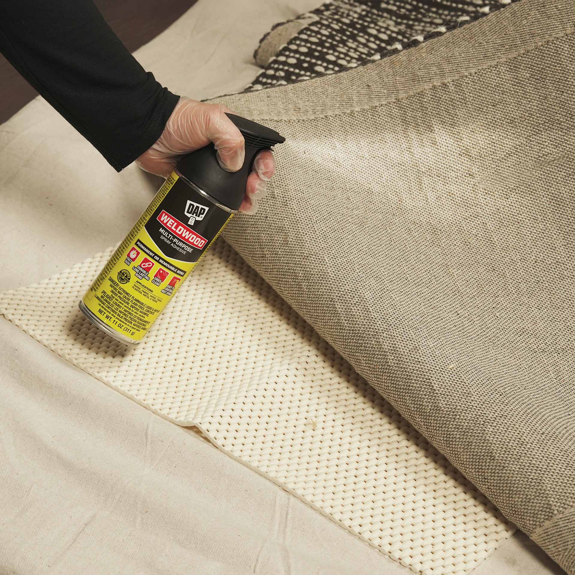 DAP Weldwood Multi-Purpose Spray Adhesive - 11 oz Can being applied to the bottom of a rug