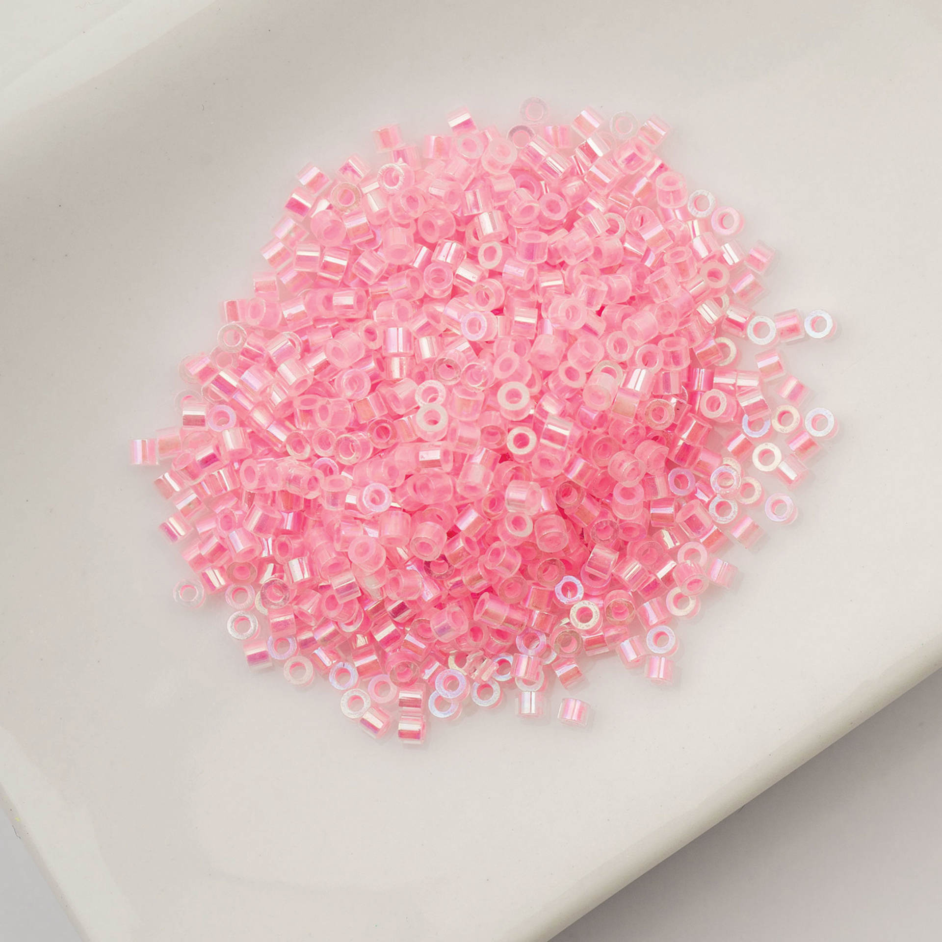 John Bead Cylin 11/0 Glow in the Dark Cylindrical Seed Beads - Rose AB, 25g sitting in dish