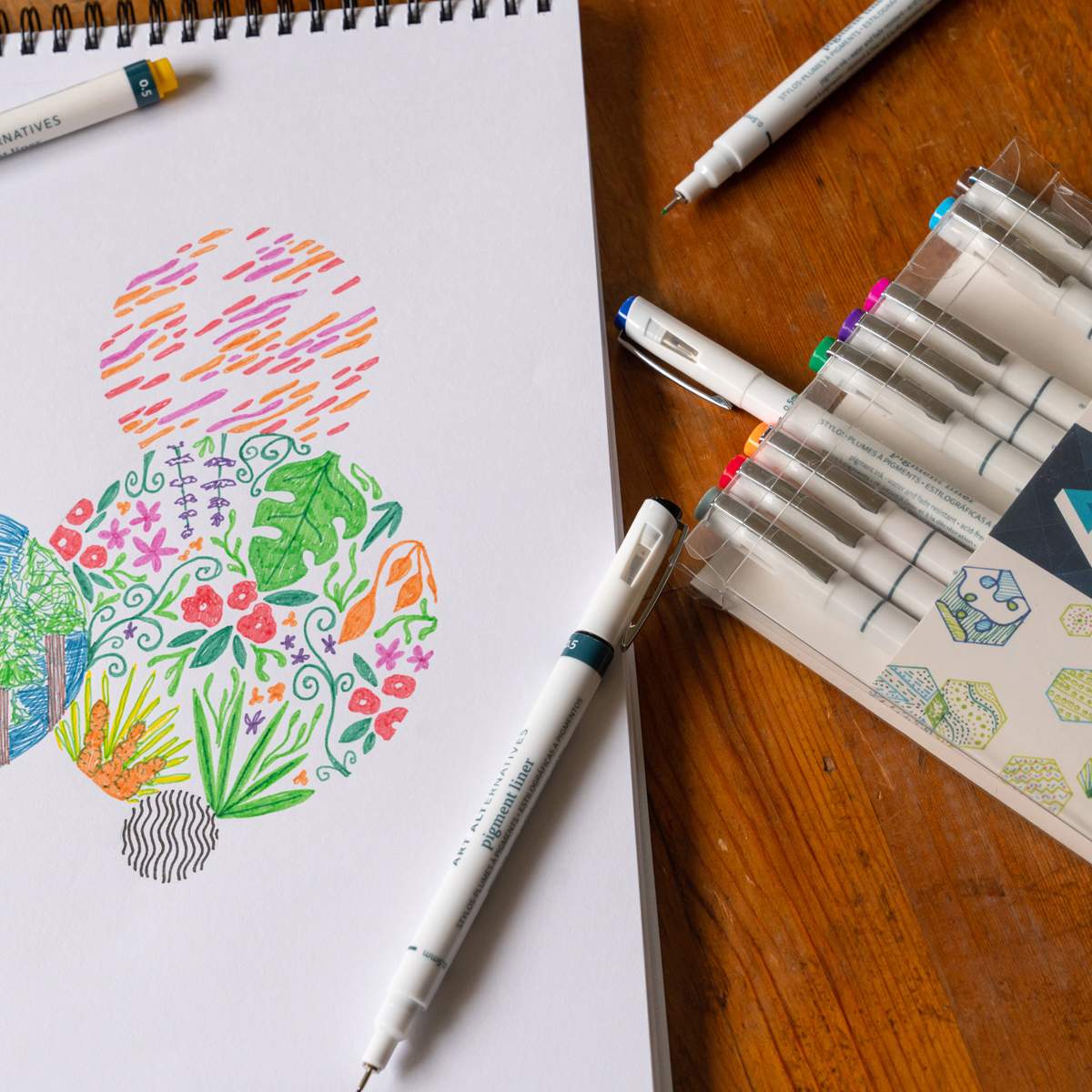 Art Alternatives Pigment Liner - Set of 12, Assorted Colors, .45 package beside illustrations