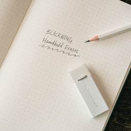 Blackwing Handheld Eraser with White Holder, on top of paper next to pencil (non included)