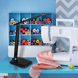 OttLite Slimline LED Desk Lamp - Black, to the left of a sewing machine