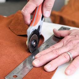 Realeather Leather Rotary Cutter, hand using blade on fabric with a ruler