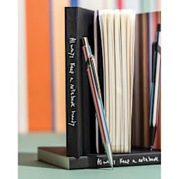 Caran d'Ache Paul Smith Special Edition 849 Mechanical Pencil - Raw Silver, 0.5 mm, propped up against a notebook